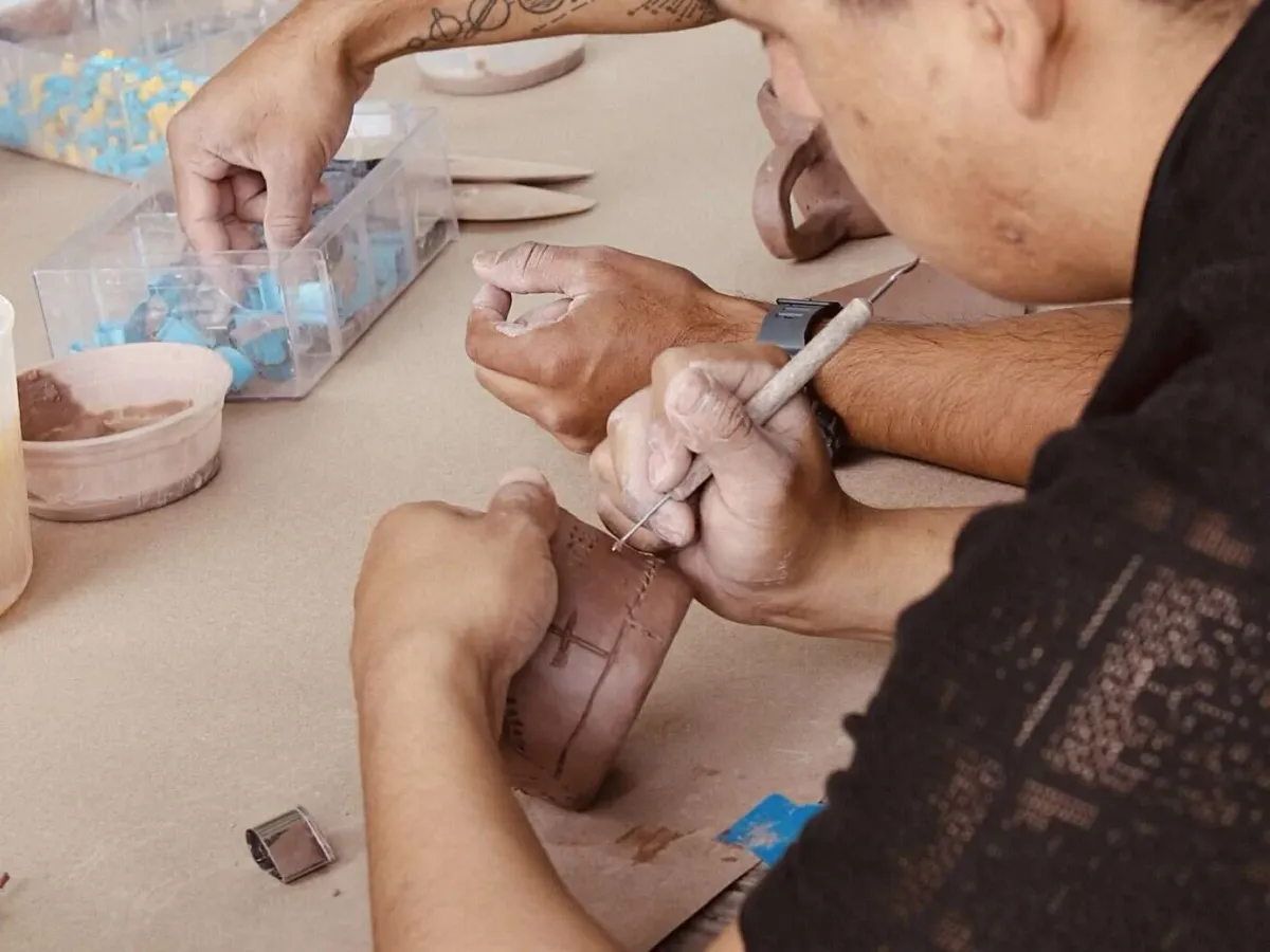 Hands scoring a clay slab with a needle tool in a beginner hand-building class at Annebrije Pottery Studio in Brownsville, TX