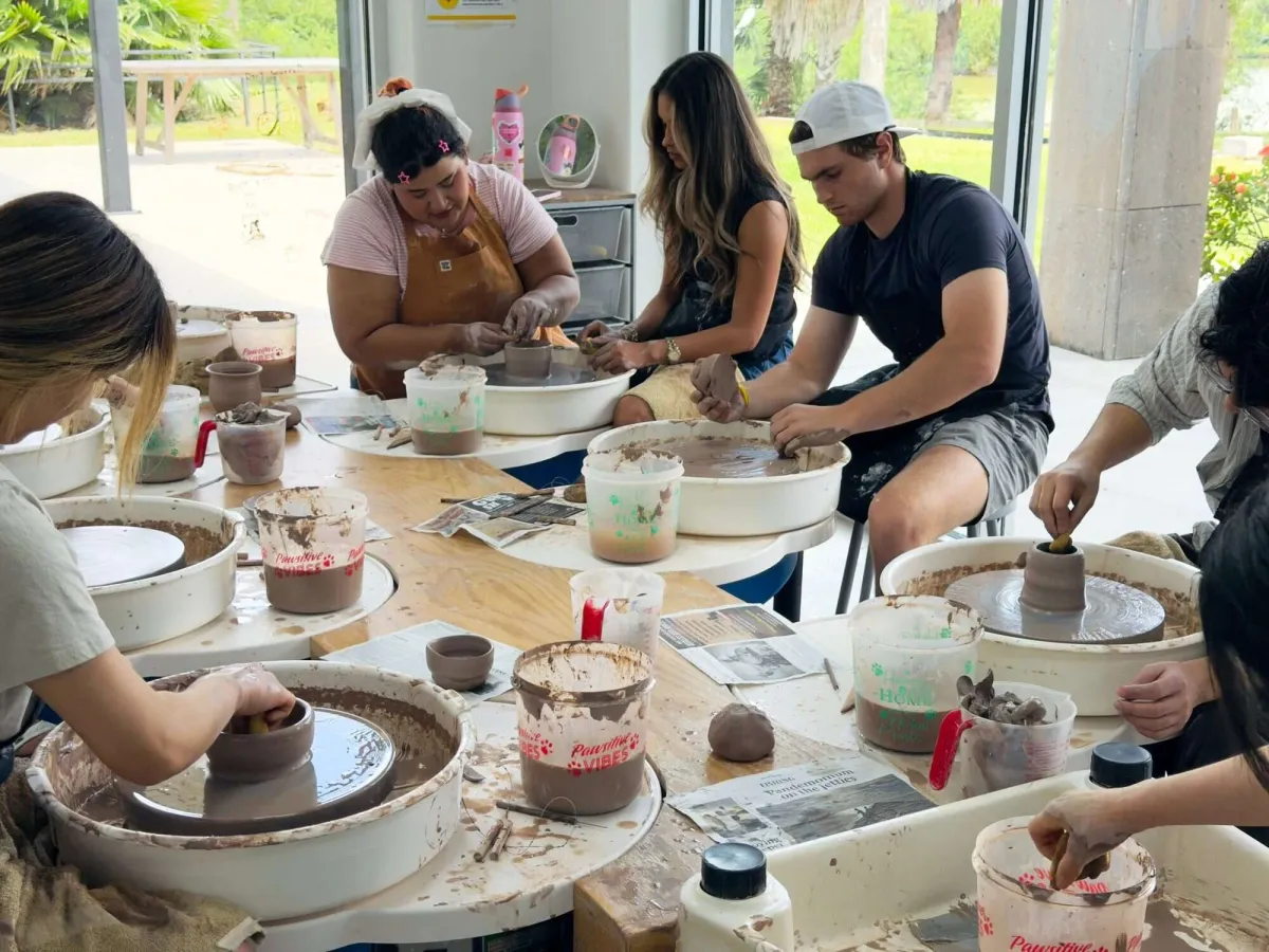 Two students laughing at their pottery wheels during a beginner wheel throwing class at Annebrije Pottery Studio in Brownsville, TX