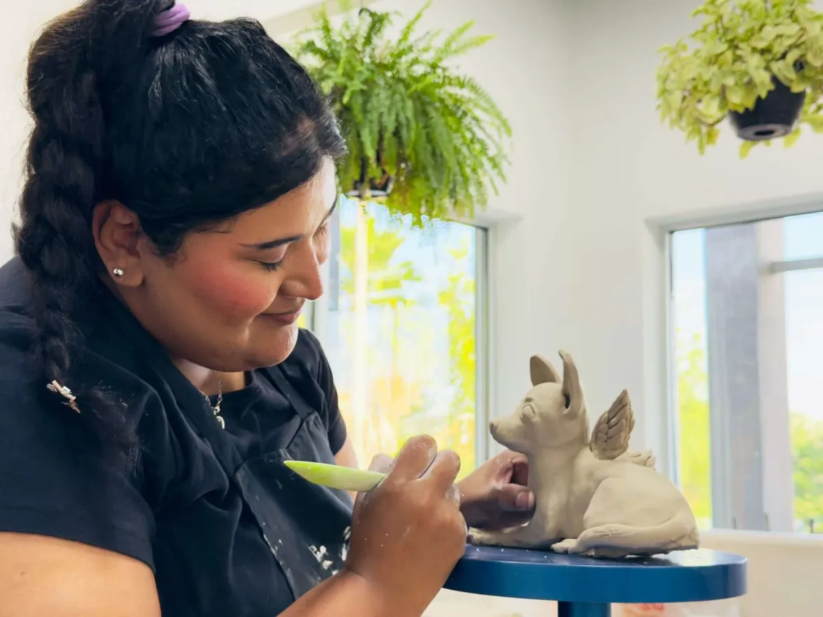 Member sculpting a winged dog figure from clay with a shaping tool at Annebrije Pottery Studio in Brownsville, TX
