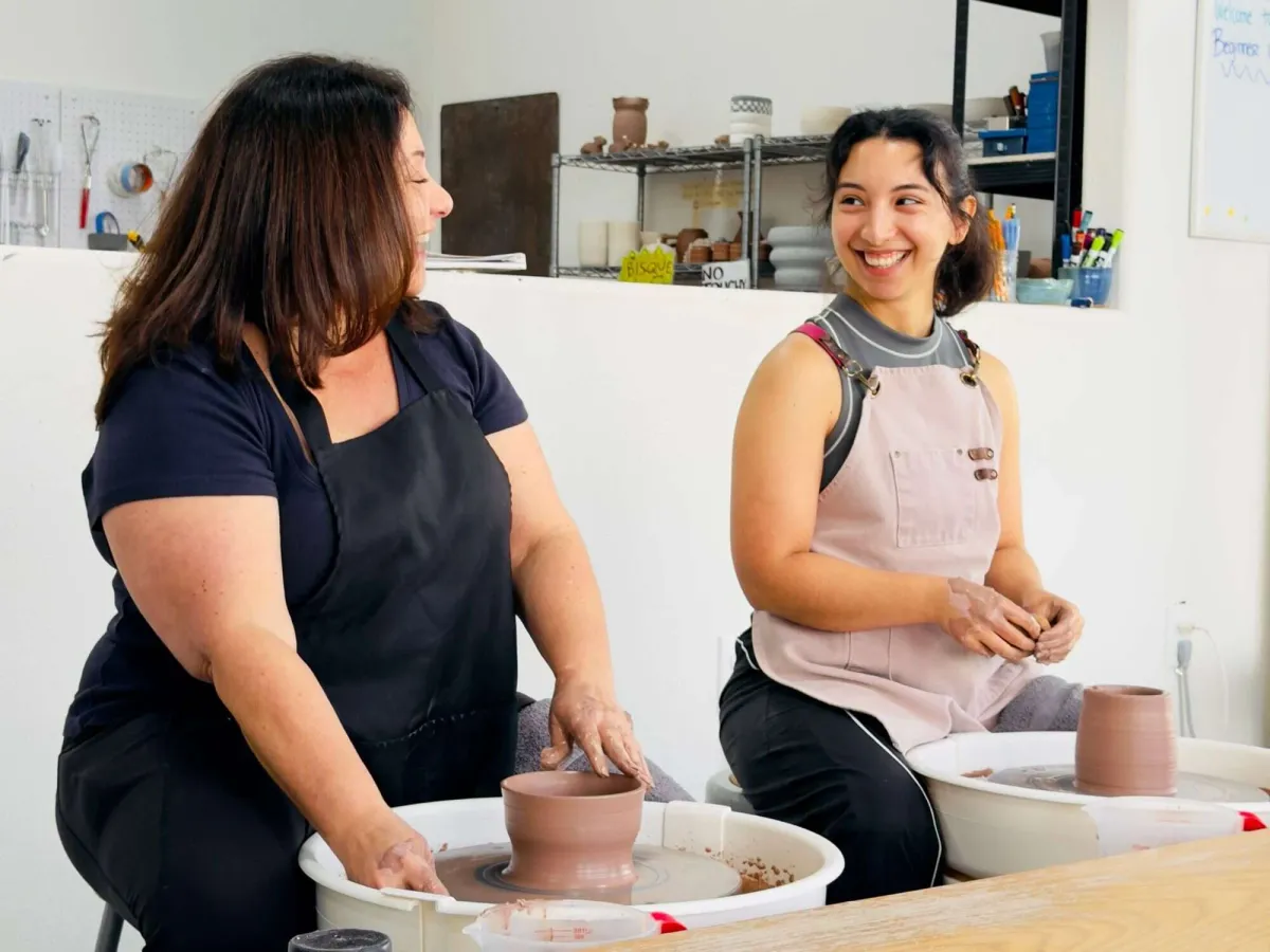 Two women laughing while throwing pottery on wheels at Annebrije Pottery Studio in Brownsville, TX